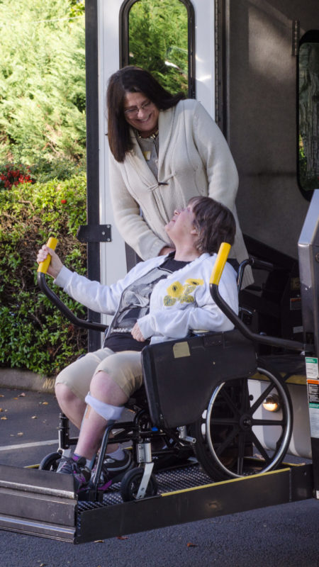 A woman in a wheelchair is helped off a van using a chair lift.